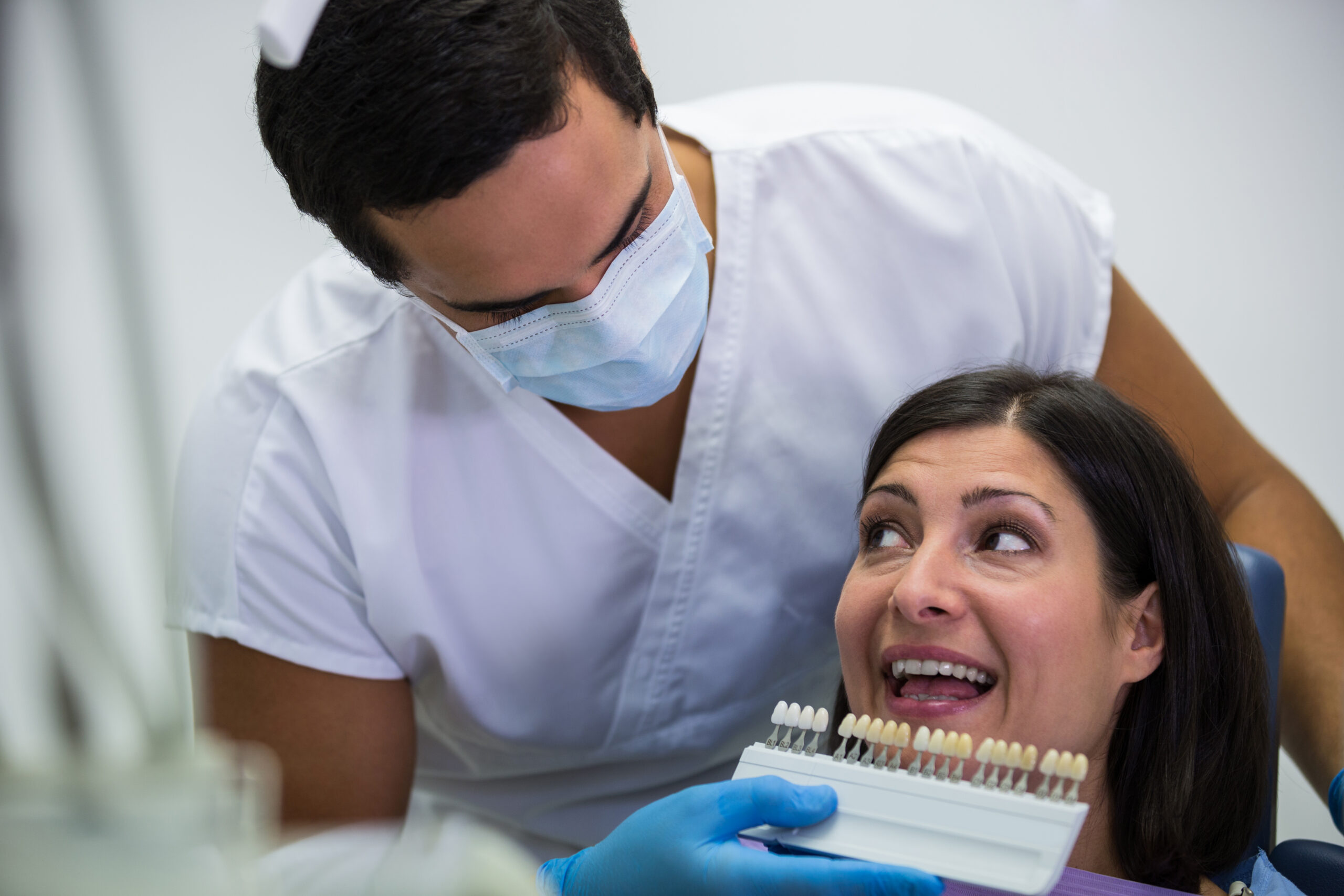 Dentist examining female patient with teeth shades at dental clinic