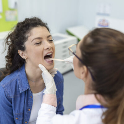 Female patient opening her mouth for the doctor to look in her throat. Otolaryngologist examines sore throat of patient. Female patient opening her mouth for the doctor to look in her throat. Otolaryngologist examines sore throat of patient.