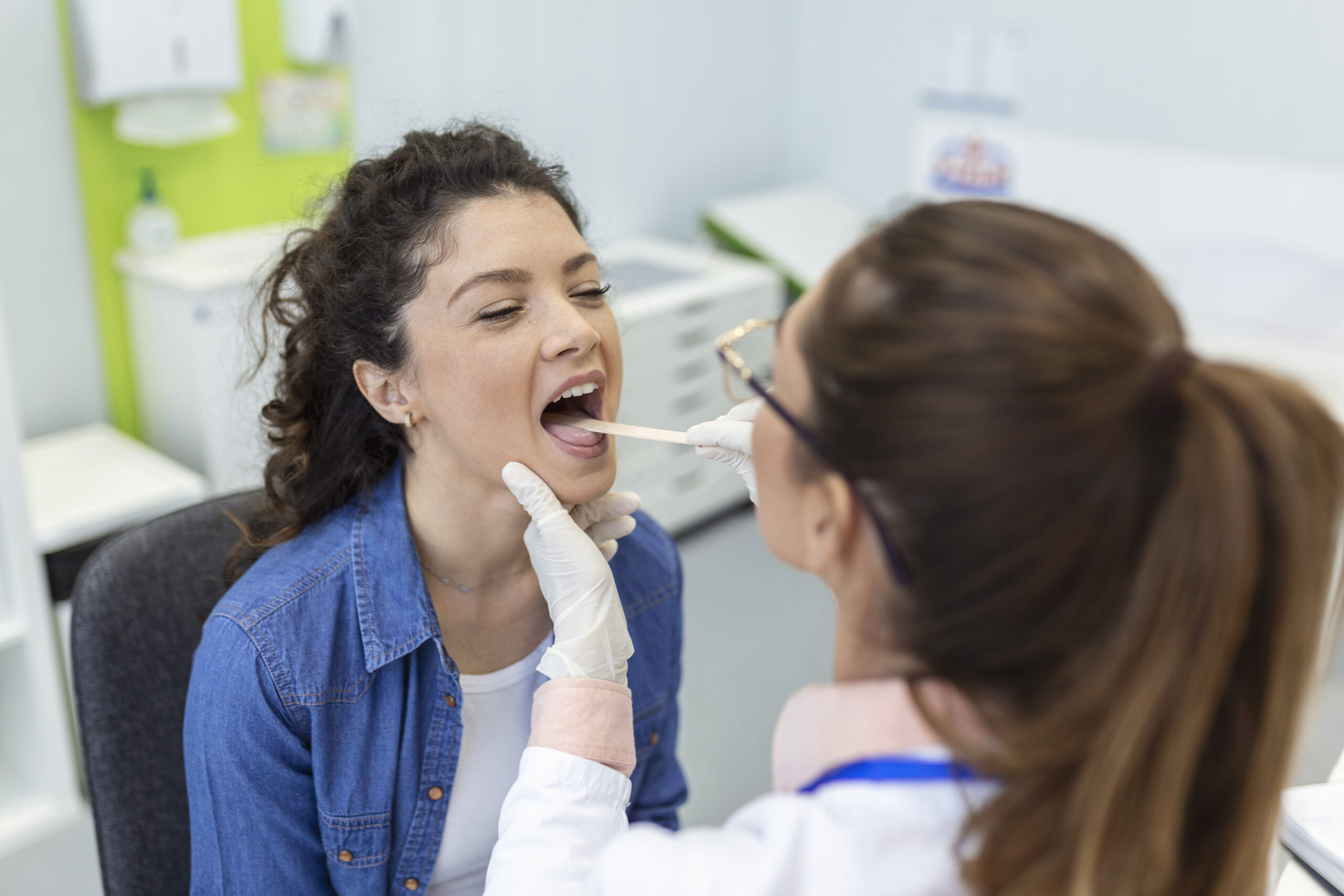 Female patient opening her mouth for the doctor to look in her throat. Otolaryngologist examines sore throat of patient.